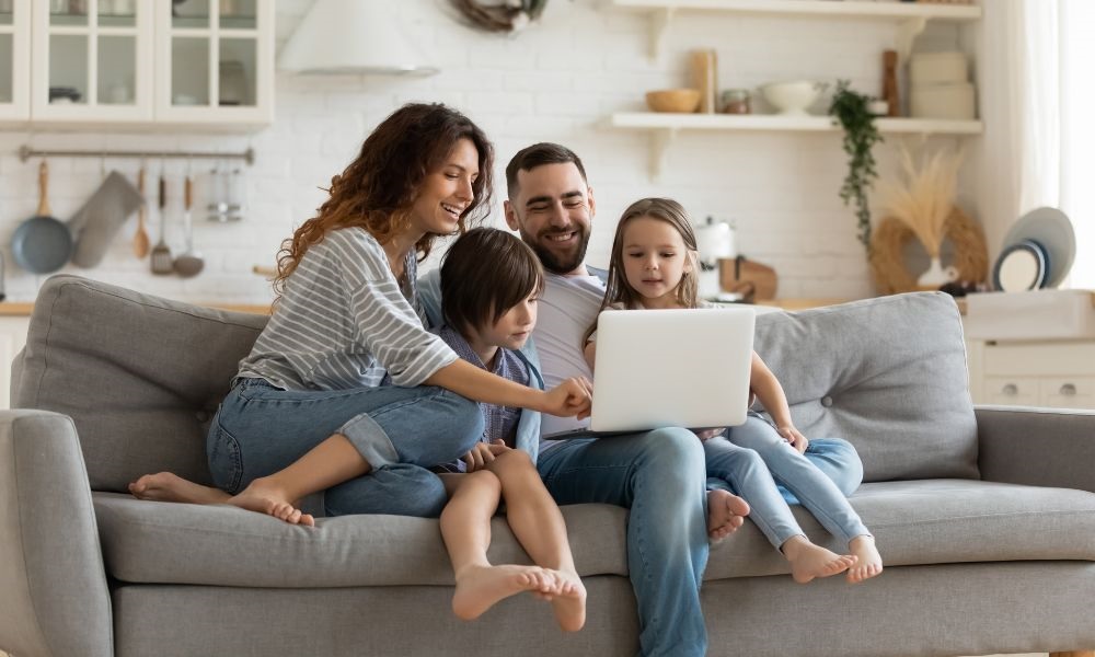 A couple and two children are sitting in the sofa and looking at the laptop computer together