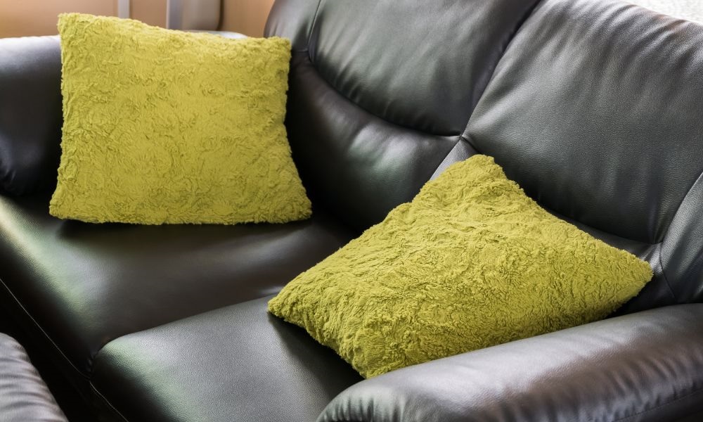 A blak leather sofa with two green cushions